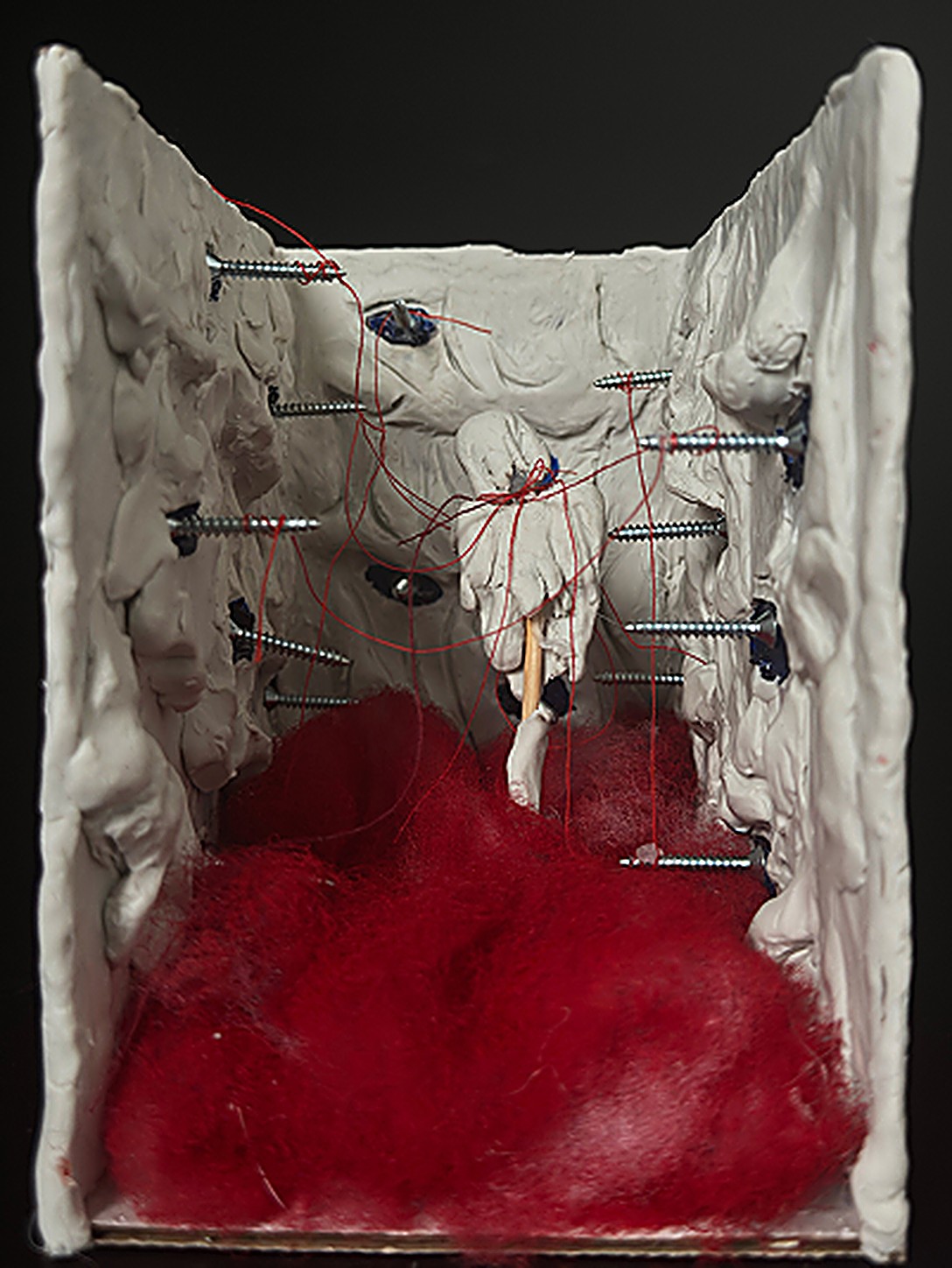 Indifference: the open white clay box, nails and red thread across its walls, red cotton pooled at its base