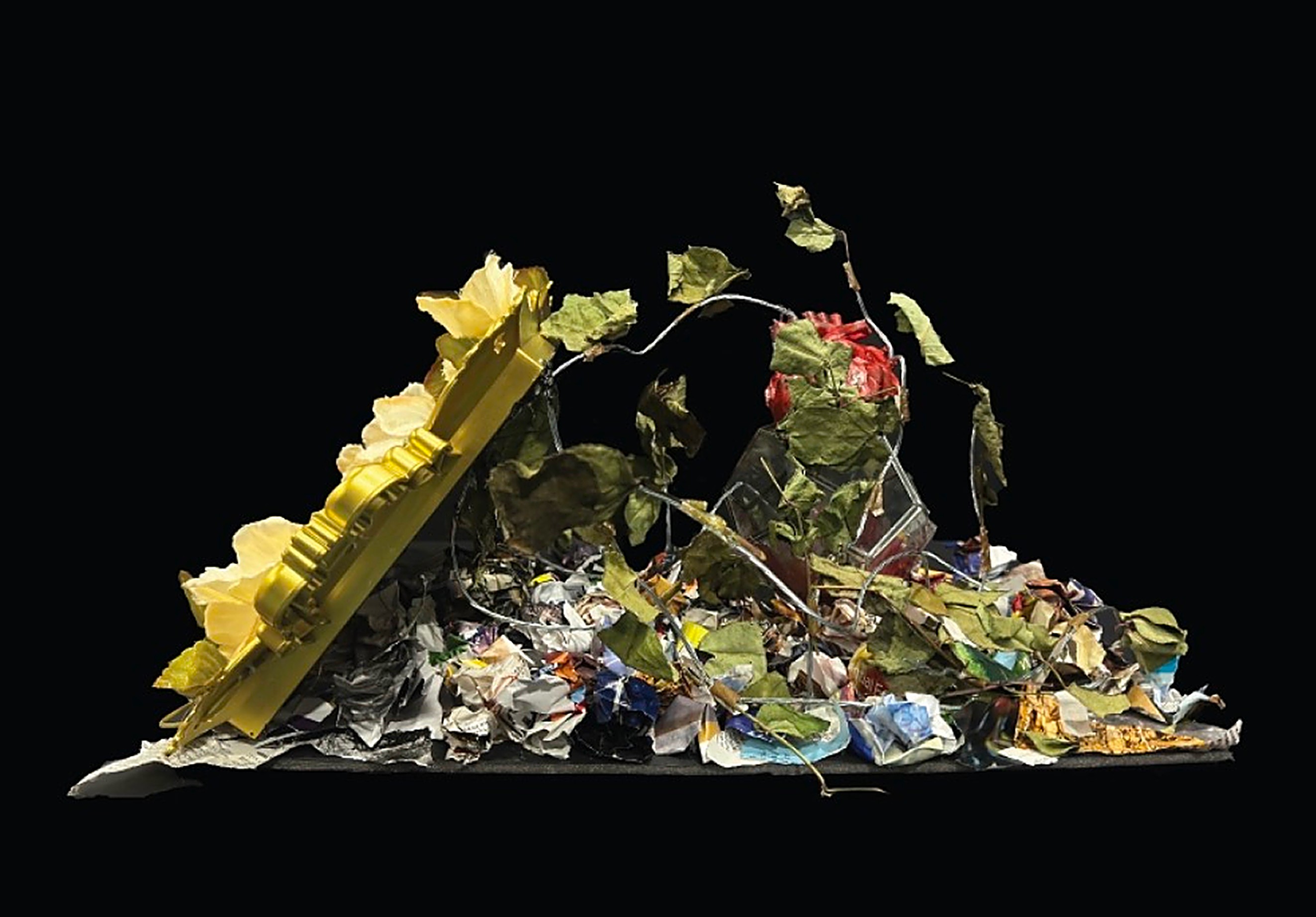 Tainted, side view: the gilded mirror leaning on a mound of newspaper, leaves and a red heart