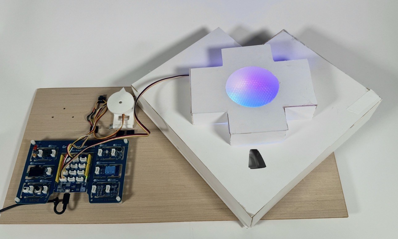 The pill dispenser on its wooden base, wiring and boards beside it, its centre glowing in rainbow colors