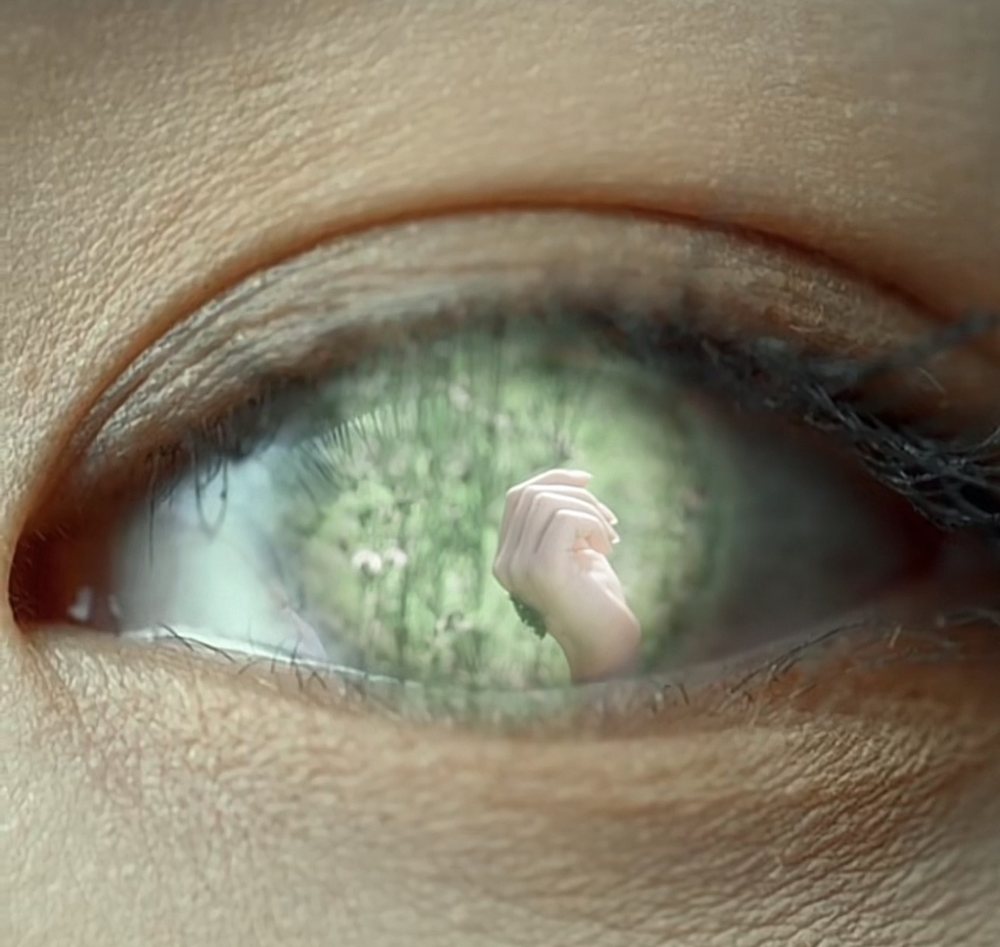 Close-up of an eye with a tiny hand reflected in its green iris