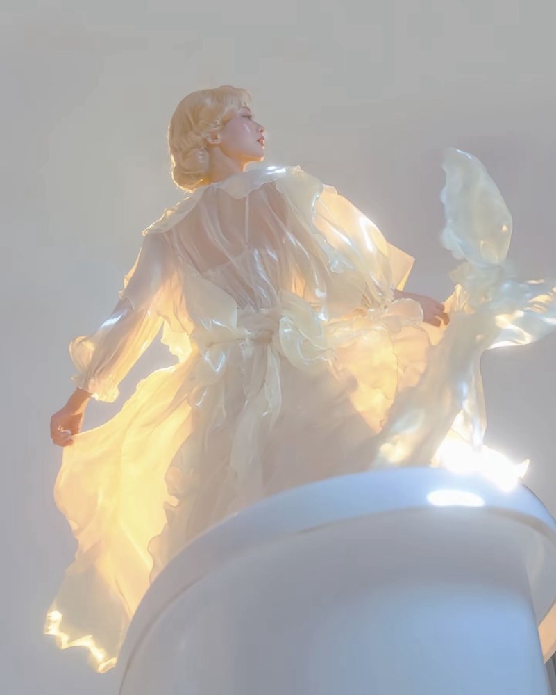 A figure in a glowing golden gown, seen from behind in soft light