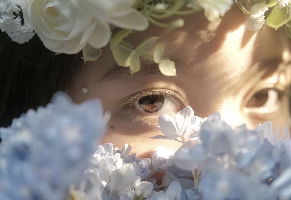 Eyes peering through blue hydrangeas under a flower crown